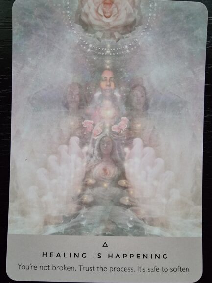 A mystical card from The Rose Oracle with ethereal, layered images of serene faces, hands, and a rose. Text at the bottom reads: HEALING IS HAPPENING. You're not broken. Trust the process. It's safe to soften.