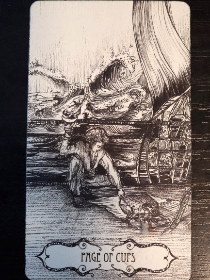 A black-and-white tarot card titled Page of Cups shows a person kneeling by water, gently touching a small sea creature. Perfect for tarot and journaling, waves rise in the background with a ship’s sail and ropes visible to the right.