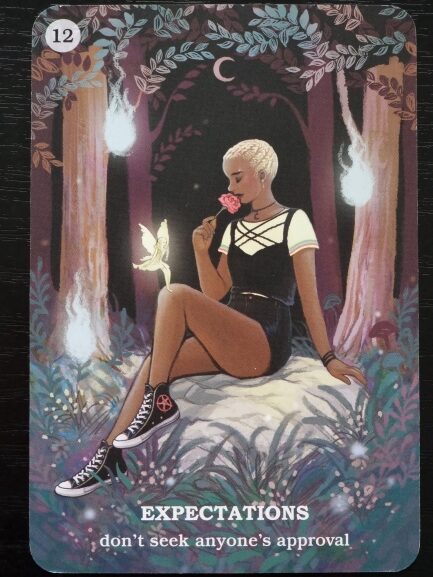 A person with short blond hair sits on a rock in a forest at night, holding a pink rose. A small glowing fairy floats nearby. The card reads: “EXPECTATIONS - don’t seek anyone’s approval.” Believe In Your Own Magic.