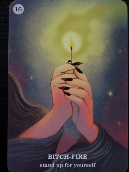 A card shows two hands with long, red nails holding a lit match against a glowing, yellow background. The card reads BITCH-FIRE stand up for yourself, drawing from Believe In Your Own Magic, and is labeled with the number 16.