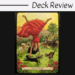 A tarot card from the Everyday Witch Oracle labeled Joy and Delight shows a woman in a red dress doing a handstand in a vibrant garden, surrounded by a dog, two cats, flowers, and a picnic setup with fruit and wine on a sunny day.