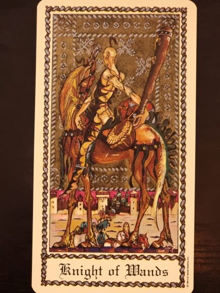 A tarot card from The Medieval Scapini Tarot titled Knight of Wands shows a knight in armor holding a wand, riding a horse. The background features a patterned border, a castle, and people near the bottom of the card.