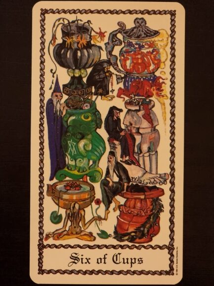 A tarot card titled Six of Cups from The Medieval Scapini Tarot shows six ornate cups stacked vertically, each filled with different objects and surrounded by various figures, including humans and animals, in a dark, surreal, and whimsical artistic style.