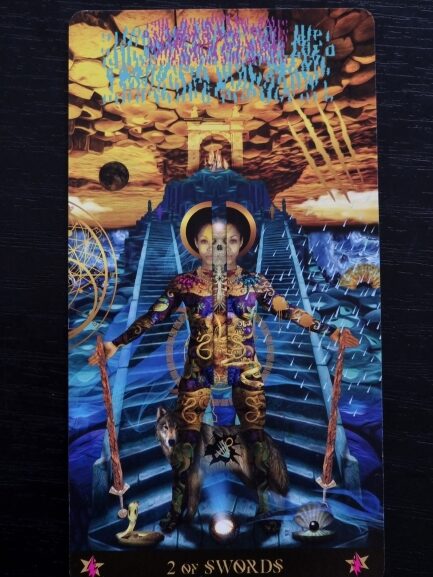 A Starman Tarot card titled 2 of Swords depicts a blindfolded figure holding two swords, standing on blue steps with cosmic and animal imagery, surrounded by water, storms, and a dramatic sky above.