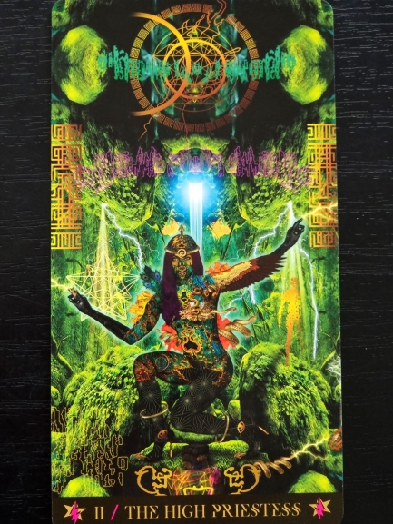 A vibrant Starman Tarot card titled II / The High Priestess depicts a seated, tattooed woman in a mystical forest, surrounded by glowing symbols and cosmic patterns, with light beams illuminating her from above.