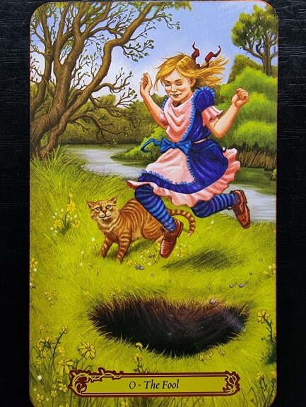 A girl in a blue and pink dress joyfully leaps over a hole in a grassy field, followed by a surprised orange cat. Trees and a river are in the background. Inspired by Tarot in Wonderland, the card reads 0 · The Fool.