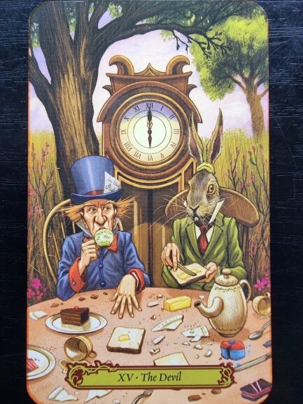 An illustrated tarot card from Tarot in Wonderland shows the Mad Hatter and March Hare having tea at a messy table, with a large clock behind them. The card is labeled XV - The Devil.