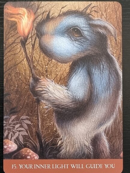 A furry blue and gray creature holding a glowing torch stands in a forest with mushrooms from Into the Lonely Woods. Text at the bottom reads: 15. YOUR INNER LIGHT WILL GUIDE YOU.