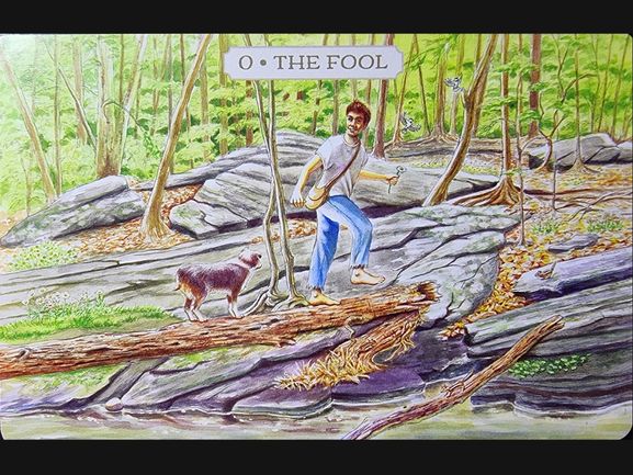 A man with a satchel walks on rocky terrain in a forest, looking upward with a joyful expression. A small dog follows him, and the card reads “0 • THE FOOL” from the Pastoral Tarot. Green trees and sunlight fill the background.