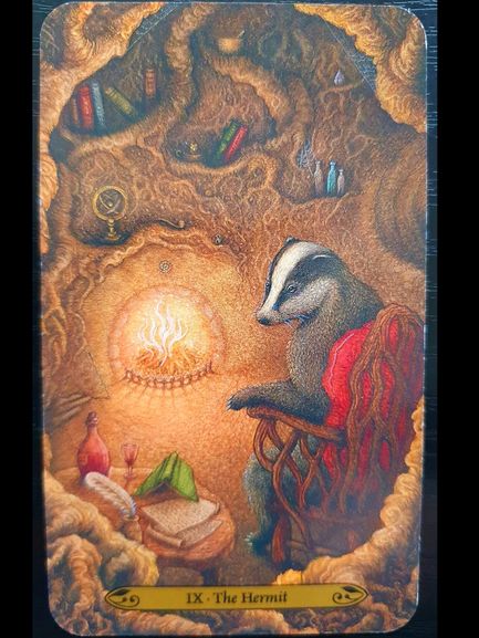 A badger sits in a cozy, lamp-lit underground burrow filled with books, objects, and writing materials. The card reads IX - The Hermit. The scene feels warm and introspective, suggesting solitude and contemplation.