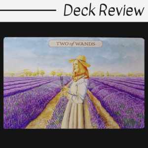 A tarot card from the Pastoral Tarot titled Two of Wands shows a woman in a hat and white dress standing in a vibrant lavender field, holding flowers, under a blue sky with distant hills.