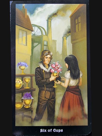 A young man in aviator goggles gives flowers to a girl in a skirt. Near golden cups filled with flowers, smoky factory chimneys and old buildings rise behind them. From The Steampunk Tarot, the card reads Six of Cups.