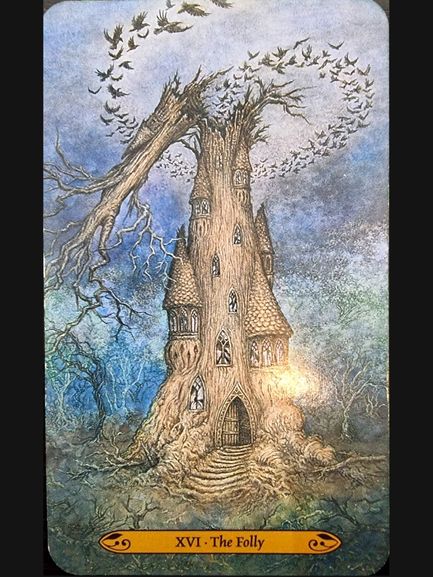 An old, tall tree shaped like a crooked tower with windows and a door stands in a barren landscape. Its top bends sideways, releasing a flock of black birds into a cloudy sky—a scene inked with the writing of fate. The card reads XVI - The Folly.