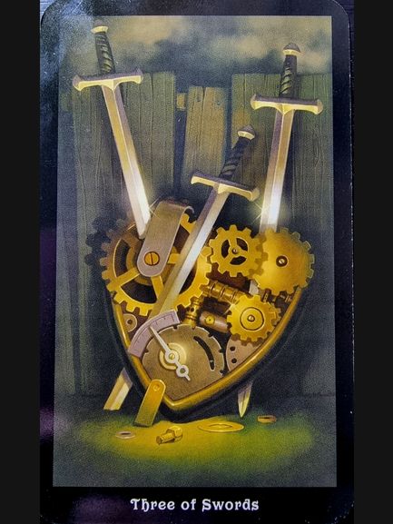 A heart-shaped arrangement of golden gears and cogs pierced by three swords, set against a wooden plank background. Inspired by The Steampunk Tarot, the image is labeled “Three of Swords” at the bottom.