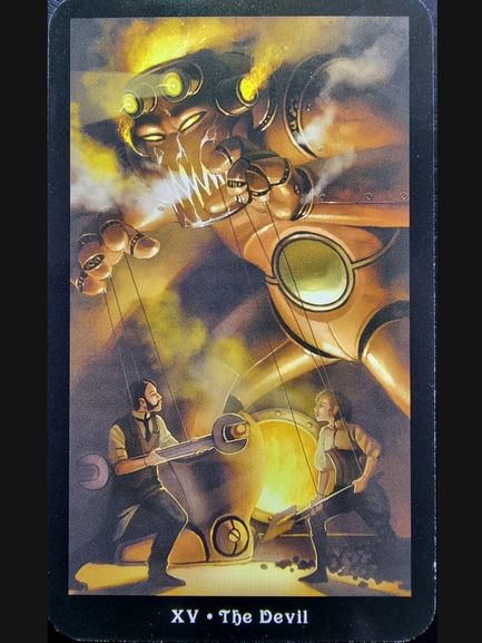 A tarot card from The Steampunk Tarot titled XV The Devil shows a large mechanical devil controlling two people like puppets with strings. The scene is fiery and intense, filled with gears and smoke in the background.