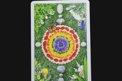 A tarot card from The Herbcrafter's Tarot, titled 21. The World - Pachamama, displays a mandala of colorful flower petals, leaves, stones, and a butterfly at its center on a grassy background. Deck Review is written above the card.
