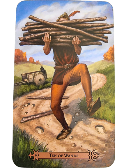 A person struggles to carry a heavy bundle of ten wooden sticks along a winding dirt path. A cart rests in the background, and autumn trees dot the landscape under a blue sky in this Modern Spellcaster's Tarot depiction of the Ten of Wands.
