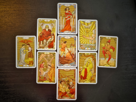 Nine tarot cards laid out in a cross formation on a dark surface, featuring detailed, colorful Art Nouveau illustrations. This striking tarot reading showcases various classic tarot figures and scenes.