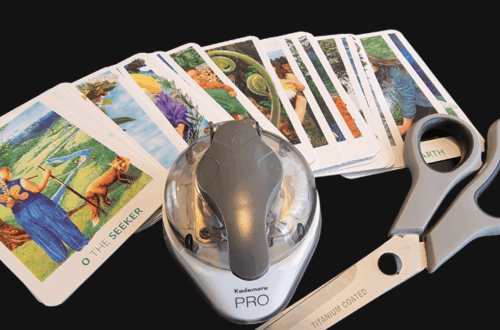 A set of tarot cards spread out with a corner rounder punch and a pair of large scissors labeled “TITANIUM COATED” on a black surface, highlighting modification. The words Deck Modification appear at the top of the image.