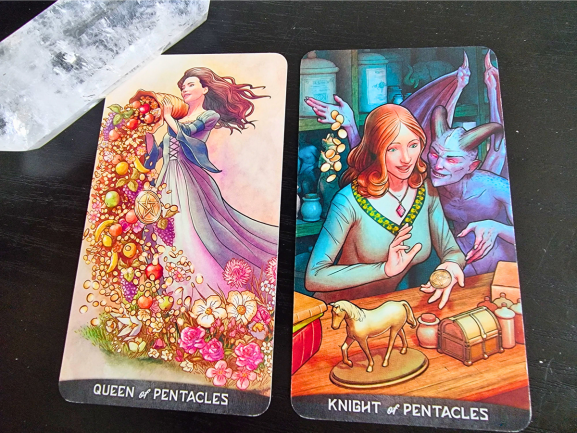 Two tarot cards on a black surface evoke the richness of A Dictionary of Symbols: The Queen of Pentacles with flowers, fruit, and gold; and the Knight of Pentacles amid coins, a toy horse, treasure chest, a smiling goblin, and a crystal in the top left.