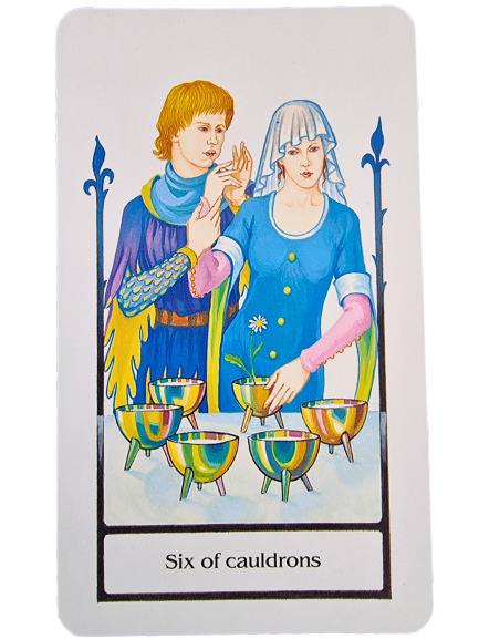 A Tarot of the Old Path card, Six of Cauldrons, shows two people in medieval clothing, one offering a flower to the other. Six cauldrons, some filled with flowers, are arranged in the foreground.