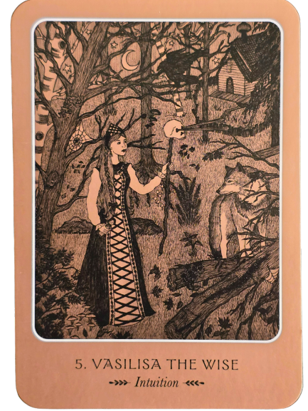 A tarot card from the Wild Woman Oracle shows a woman in a patterned dress and crown holding a staff topped with a skull, standing in a dark forest. In the background is a house on chicken legs. The card reads: 5. Vasilisa the Wise – Intuition.