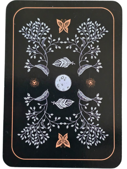 A decorative card back inspired by the Wild Woman Oracle, featuring white branches, leaves, and two birds, with a central moon, two orange butterflies, and hearts. The symmetrical design stands out on a black background with an orange border.