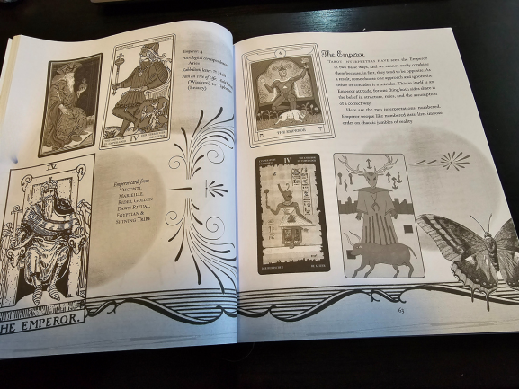 An open book displays Tarot Wisdom with illustrations and descriptions of The Emperor tarot card, featuring various artistic interpretations, decorative borders, and a large butterfly illustration on the bottom right page.
