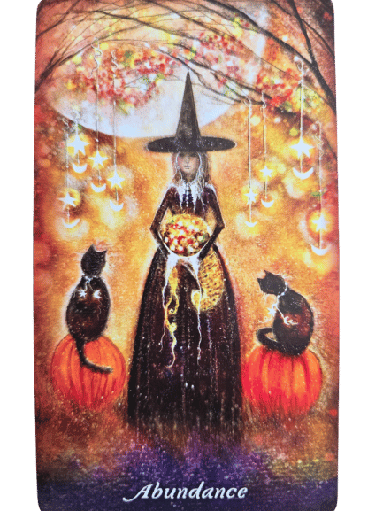A witch in a black hat holds glowing coins under autumn trees with hanging lights. Two black cats sit on pumpkins. “Abundance” and Earthly Souls and Spirits Moon Oracle appear below as the scene glows with golden, magical light.
