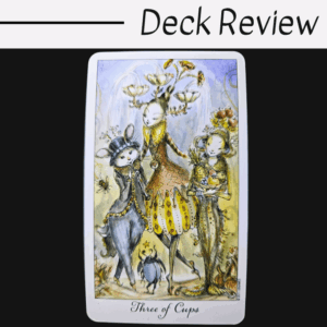 A whimsical tarot card from the Joie de Vivre Tarot labeled Three of Cups features three fanciful, animal-like characters in colorful attire, standing together against a soft, pastel background. Text above reads Deck Review on a white and black backdrop.