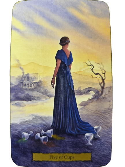 A woman in a flowing blue dress stands by a river, looking away towards a distant house. Five cups, three tipped over, lie at her feet. The misty background and barren tree evoke the Tarot of the Witch's Garden atmosphere.