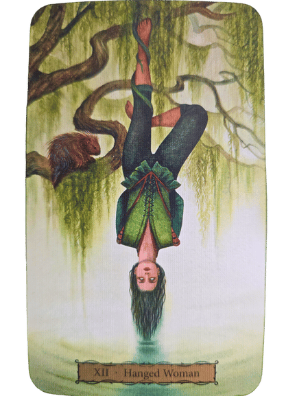 A Tarot of the Witch's Garden card labeled XII - Hanged Woman shows a woman hanging upside down from a tree branch by one leg, her green dress and loose hair flowing gracefully toward the ground.