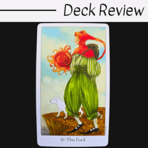 A tarot card from the Dreaming Way Tarot, titled 0 The Fool, shows a colorfully dressed figure with a red hat and green clothes standing on a cliff with a small white dog. The bright blue sky sets the scene. Deck Review text is above.
