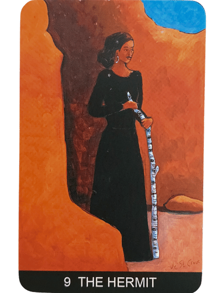 A woman in a long black dress stands between orange rock formations, holding a white and blue staff. She looks to the side. The card reads 9 THE HERMIT at the bottom, from the Tarot de St. Croix deck.