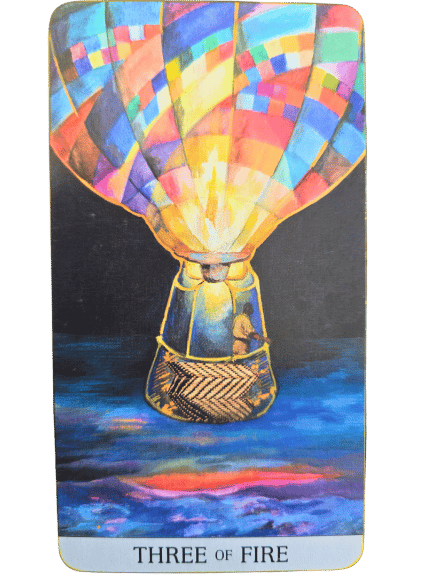 A tarot card from the Japaridze Tarot labeled Three of Fire shows a brightly colored hot air balloon with two figures in the basket, floating above a vibrant, multicolored landscape under a dark sky.