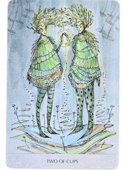 Two figures in green, leaf-like outfits stand facing each other, touching hands as light glows between them. Adorned with leafy crowns and surrounded by delicate plants, they embody the Magicmakers Tarot’s enchanting spirit. Text below reads TWO OF CUPS.