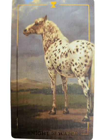 A tarot card from the Folkloric Forest Tarot featuring a white horse with black spots standing on grass under a cloudy sky. The card has yellow borders and the text KNIGHT OF WANDS at the bottom.