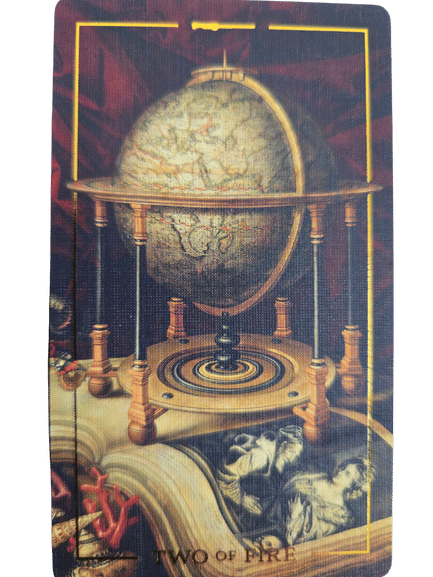 A tarot card from the Folkloric Forest Tarot, the Two of Fire depicts a vintage globe in a wooden frame atop an open book with illustrations, all surrounded by reddish, fiery tones.